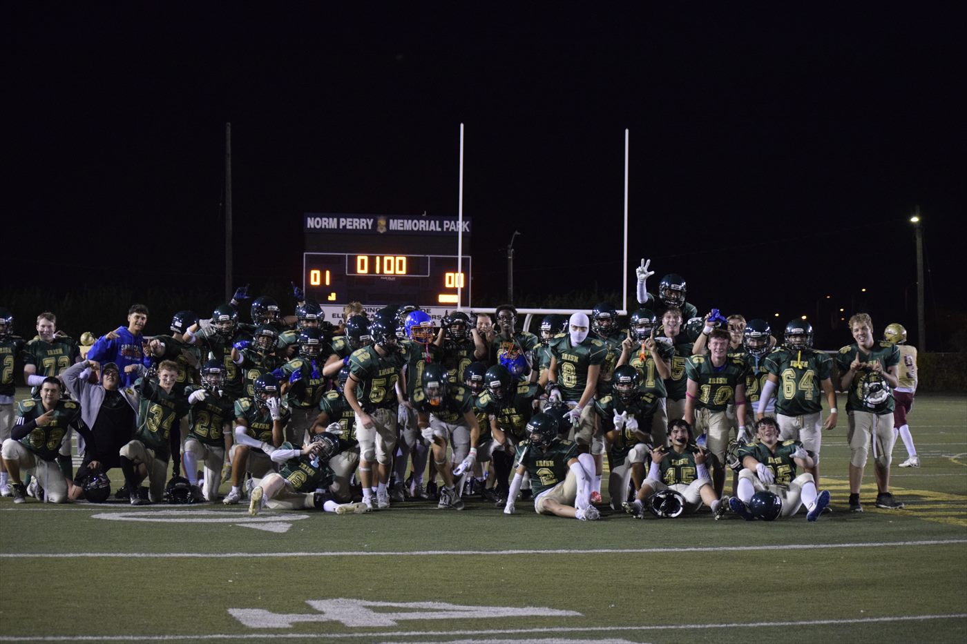 Football team gathered for a group photograph beneath the scoreboard.
